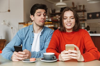 Image of happy woman holding mobile phone in cafe while curious man looking at her smartphone with interest