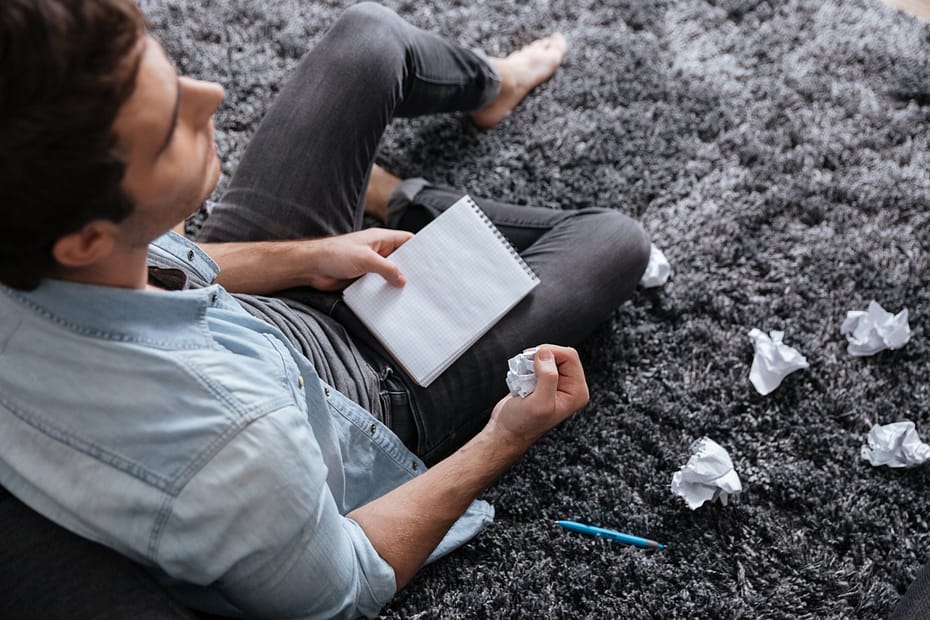 man-holding-crumpled-paper-and-notepad-while-sitting-on-carpet-2
